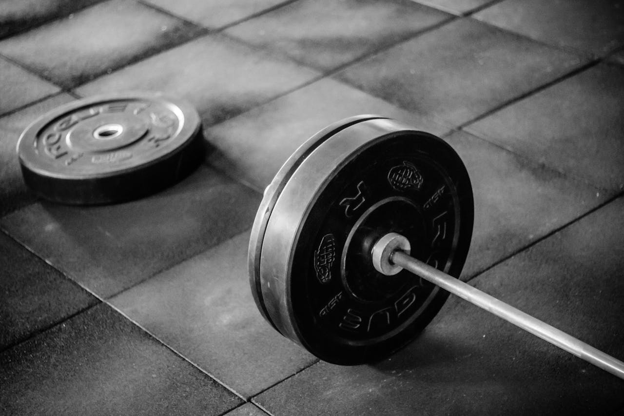 Grayscale image of heavy gym barbell and weights on rubber mat flooring.
